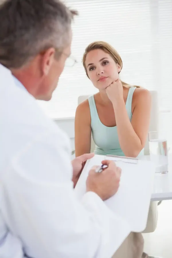 Eine besorgte junge Frau hört aufmerksam zu, während ein Arzt in einem weißen Kittel während einer Konsultation Notizen auf einem Klemmbrett macht